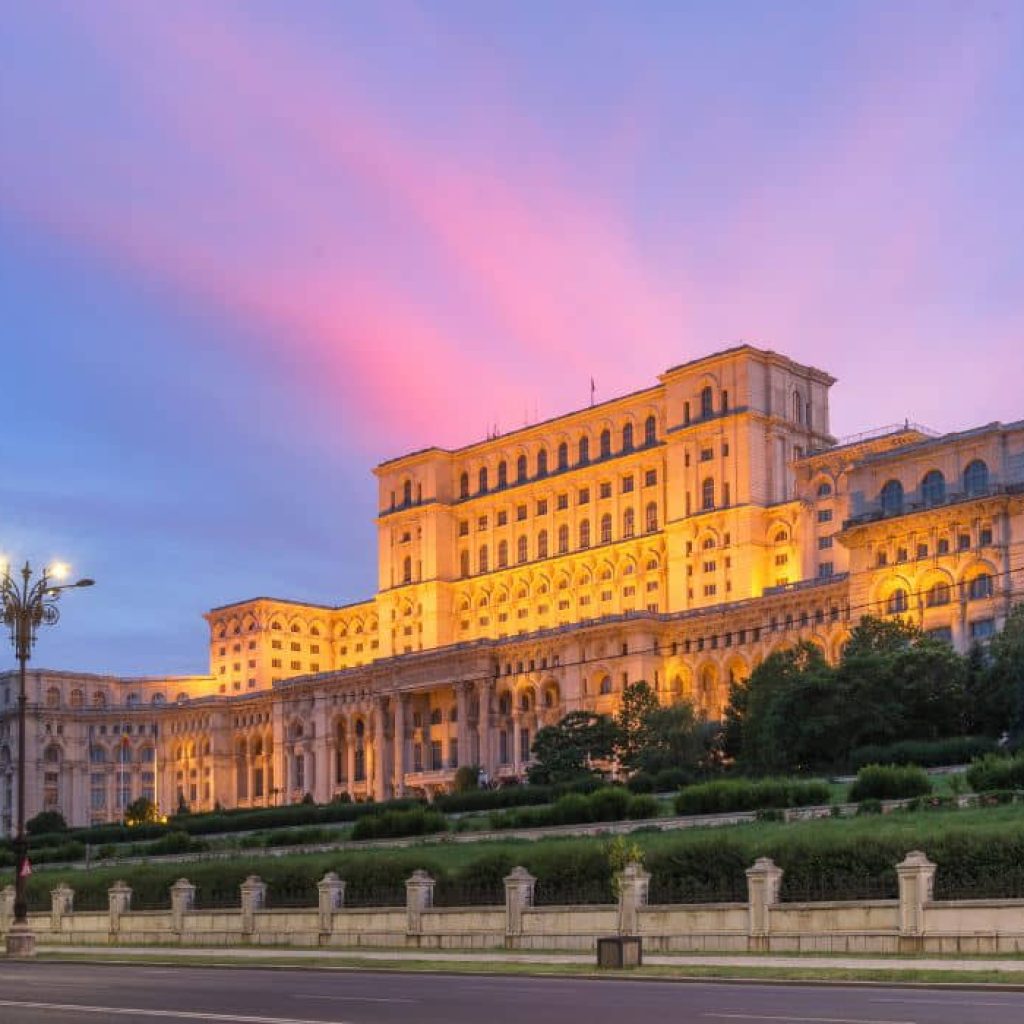 Palace of Parliament in Bucharest illuminated at dusk with dramatic purple and pink sky, Romania's massive government building