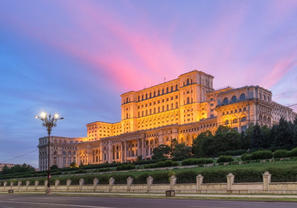 Palace of Parliament in Bucharest illuminated at dusk with dramatic purple and pink sky, Romania's massive government building