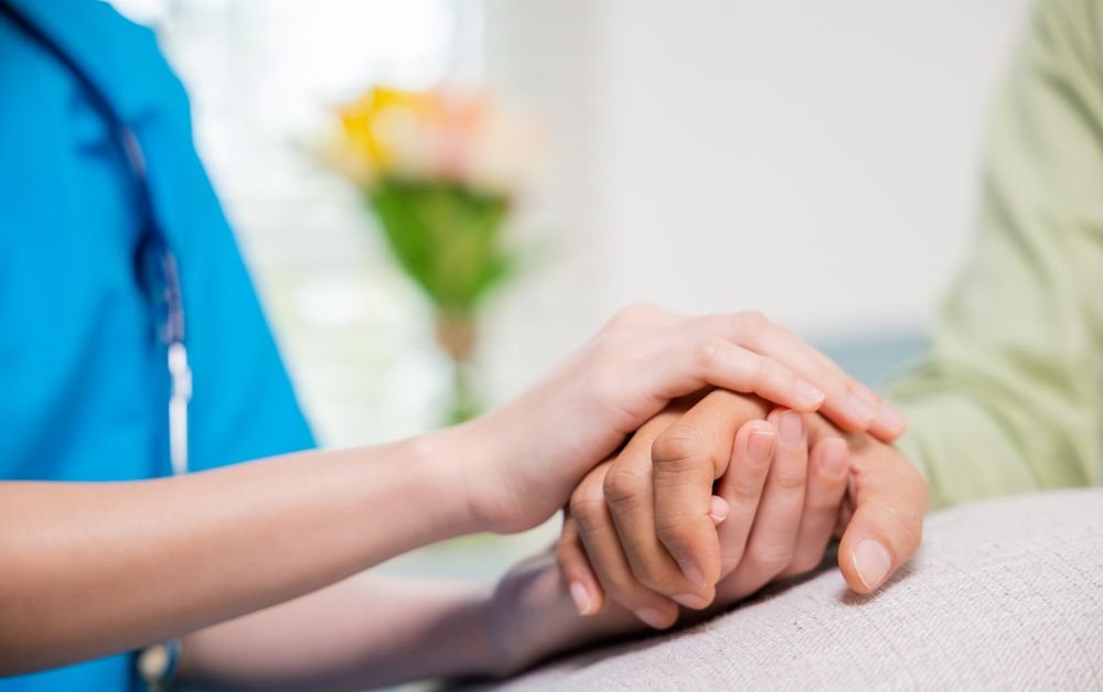 An image of a nurse holding a retirees hand for an article about aged care reform 2025.