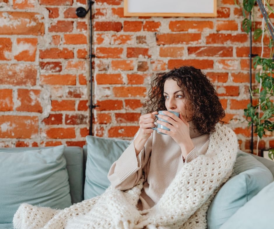 an adult woman wrapped in a cozy throw blanket sipping her coffee